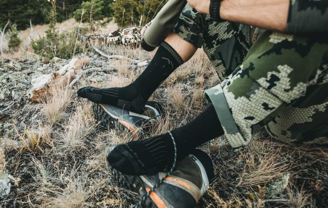 Hunter in camo taking a break while wearing midweight hunting socks in black
