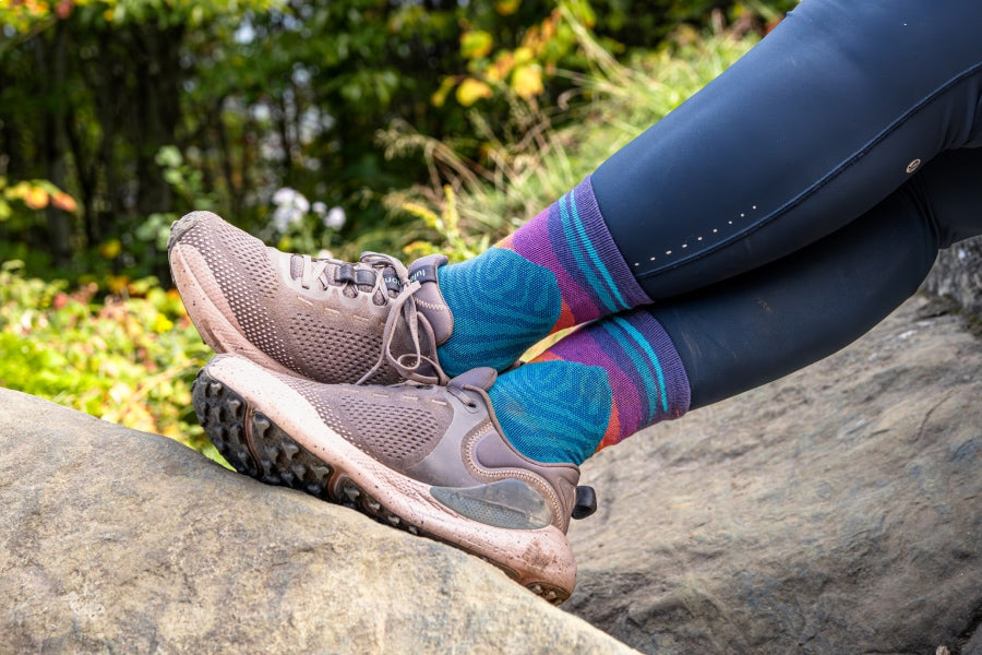 Feet wearing the MIrnavated running sock, a sock with a mountain design in blues, purples, and peaches. 