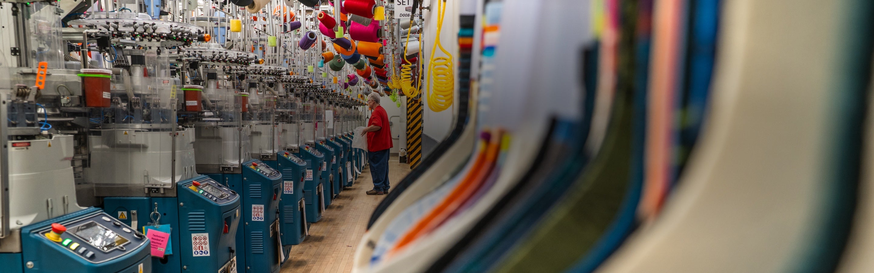 A view down a row of knitting machines at the Darn Tough Northfield Mill, with a view of the golden sock samples