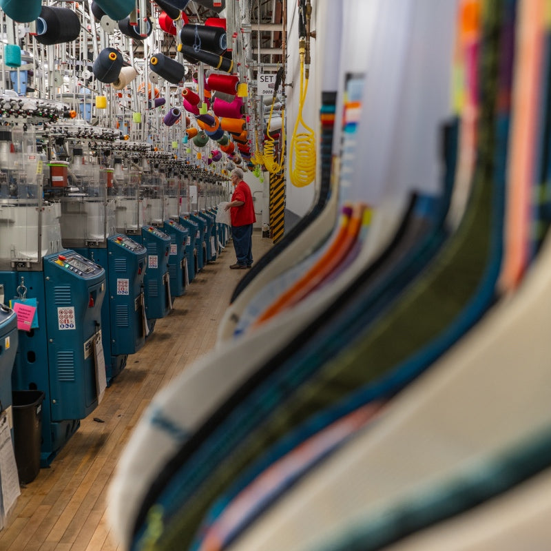 A view down a row of knitting machines at the Darn Tough Northfield Mill, with a view of the golden sock samples