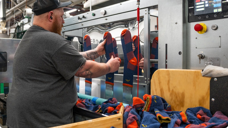 A man placing a sock onto a metal foot form so it can pass through the boarding machine 