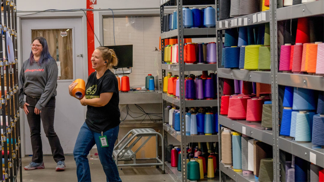 An employee laughing as she holds a yarn cone she's just taken off the chock-full shelf