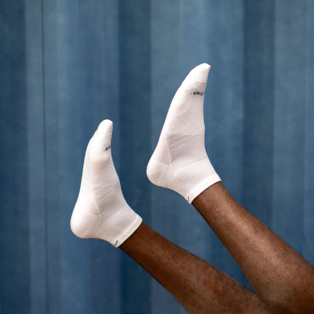 Model laying down with their feet in the air wearing men's coolmax quarter running socks in whitte with a blue background